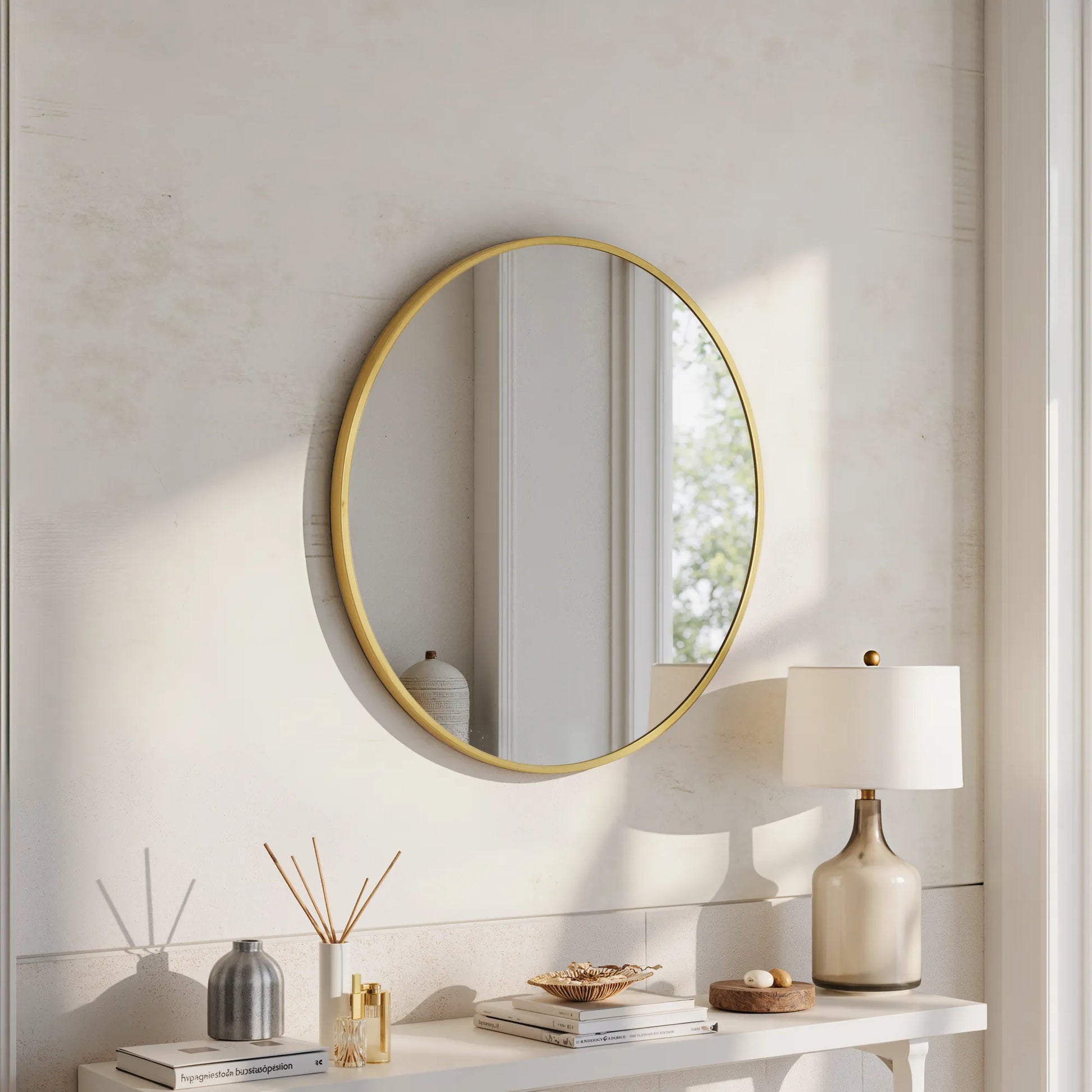 Sylvie gold round wall mirror above a white console with a table lamp and reed diffuser in a bright room