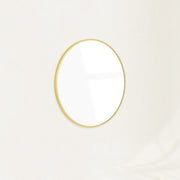 Sylvie round wall mirror with a slim gold frame mounted on a plain wall