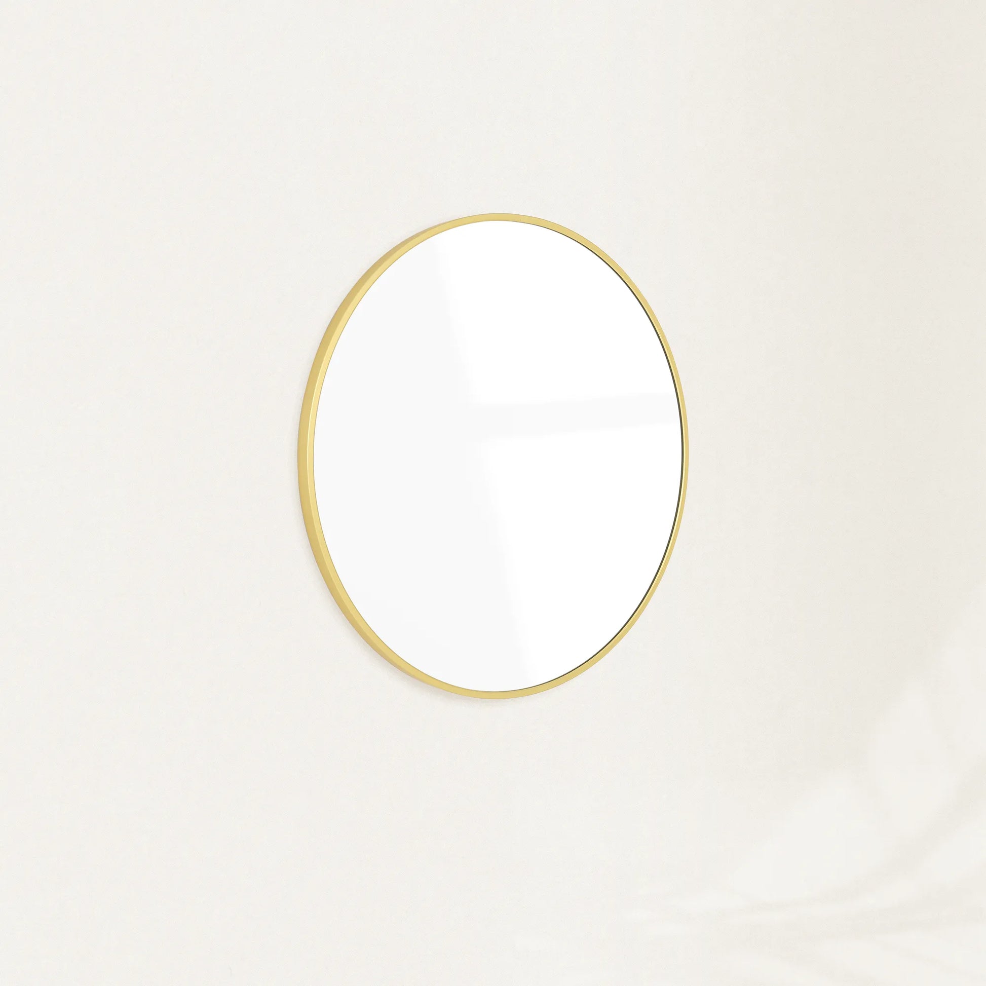 Sylvie round wall mirror with a slim gold frame mounted on a plain wall